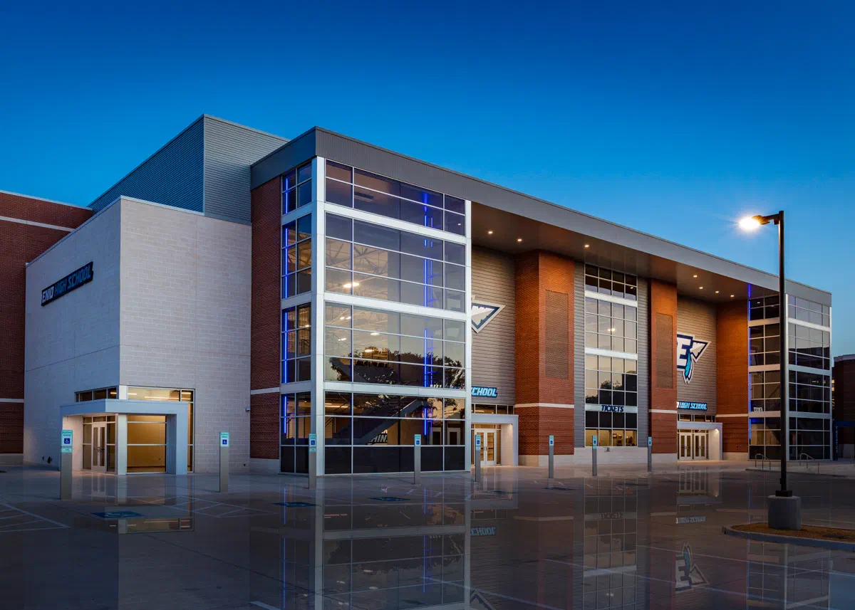 Enid High School gymnasium and performing arts center exterior at dusk with glass curtain wall