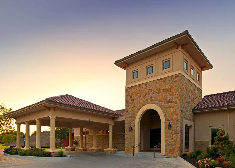Oakwood Country Club clubhouse with stone tower, arched entry and tile roof at sunset