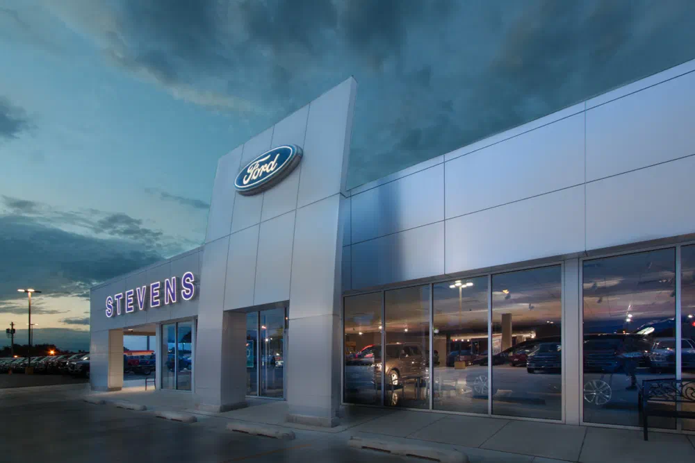 Stevens Ford dealership with aluminum composite entry portal and glass showroom at dusk